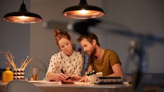 Elegantes luminarias LED colgantes que proyectan WarmGlow sobre la pareja que trabaja junta, mostrando una iluminación energéticamente eficiente para tareas nocturnas productivas.