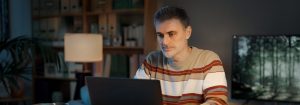 Un hombre que lleva un jersey a rayas se sienta en su escritorio y está mirando la computadora portátil frente a él