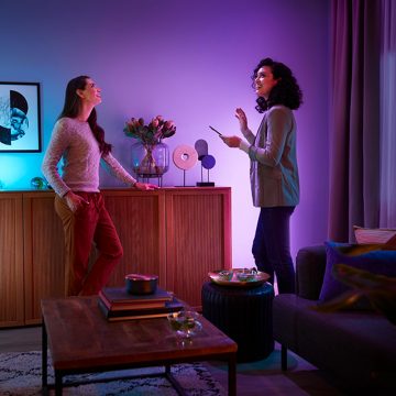 Een vrouw stelt in de Philips Hue app op haar smartphone een kleurvolle lichtscène in met roze en paars licht in een woonkamer. 