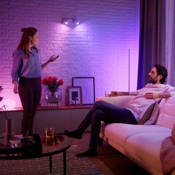 A couple relax in their living room with Philips Hue Christmas lighting that fills their space with shades of blue and purple smart light.