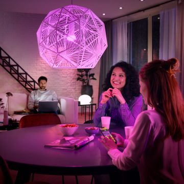 Eine Dame erzeugt mit der Philips Hue App auf ihrem Smartphone eine farbenfrohe Lichtszene in Rosa und Lila an einem Esstisch. 