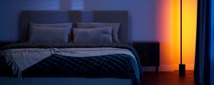 En Philips Hue Signe gradient gulvlampe, der er på tilbud på Black Friday, kaster gule og lyserøde nuancer af intelligent lys på en seng.