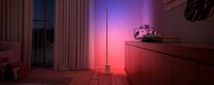 Een Philips Hue Signe gradient vloerlamp, verkrijgbaar tijdens de Black Friday deals, verlicht een muur met roze en blauwe tinten slim licht.