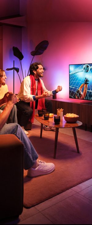 A group of friends celebrate a goal seen on a TV football match with the Hue Sports Live feature making lights react to the moment in tones of pink and blue.