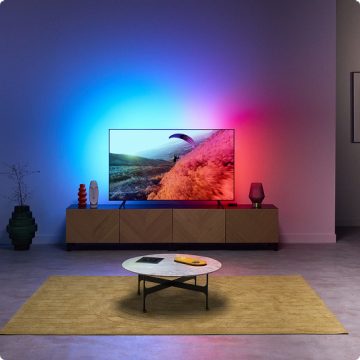Un soggiorno con luce immersiva proveniente dalla retroilluminazione della TV, sincronizzata con i colori dello schermo TV.