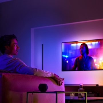 Homme sur un canapé regardant la télévision avec un éclairage et un haut-parleur intelligent surround sur la table d'appoint à côté de lui