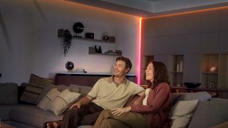 Een stel zit op een bank in een woonkamer met hoeken en plafondlijnen, die direct worden verlicht door LED strips. 