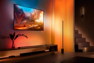 Een Signe gradient vloerlamp naast een tv met een meeslepende entertainmentverlichting die smart oranje lichttonen uitstraalt. 