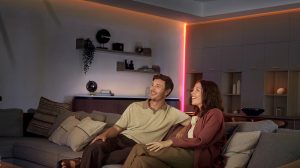 Een stel zit op een bank in een woonkamer met hoeken en plafondlijnen, die direct worden verlicht door LED strips. 