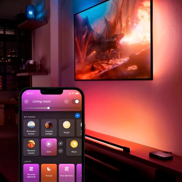 A TV surround lighting setup glowing in tones of blue and pink controlled by the Hue app showing different light scenes.
