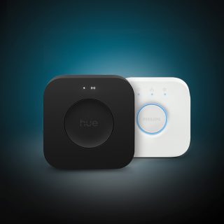 New Hue Bridge Pro and Philips Hue Bridge smart home lighting control systems. A person controlling Philips Hu smart lighting using the Hue app on a smart phone. A white Philips Hue smart button placed on a table next to a laptop computer.