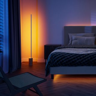 Vertical smart floor lamp placed in the bedroom corner, casting orange light onto walls and floor near bed and nightstand.