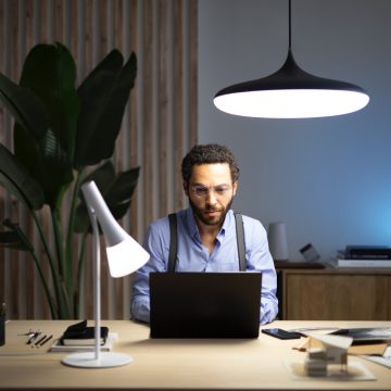 Hombre sentado frente a una computadora portátil en un escritorio con dos lámparas inteligentes