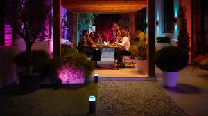 Four adults seated at an outdoor dining table with purple and blue low-voltage lighting