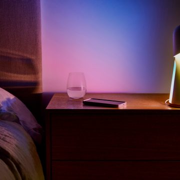 A bedside table with a glass of water, a smartphone, and a lamp casting colored light onto the wall and surface.