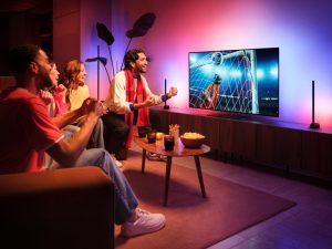 A group of friends celebrate a goal seen on a TV football match with the Hue Sports Live feature making lights react to the moment in tones of pink and blue.