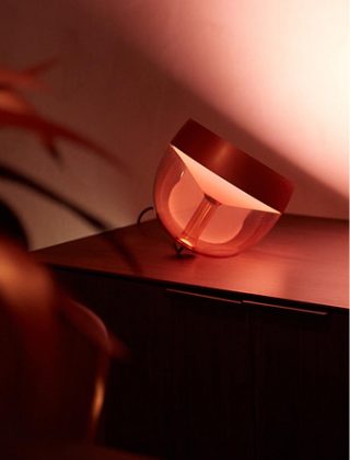 A Philips Hue Iris table lamp glowing in a warm tone of white light. 