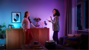 Two people are talking in a living room illuminated by colorful smart lighting, with decorative lights highlighting the space.
