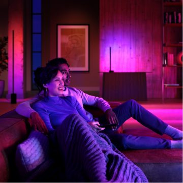 Two people relaxing on a sofa in a living room, illuminated by vibrant purple and pink smart lighting.