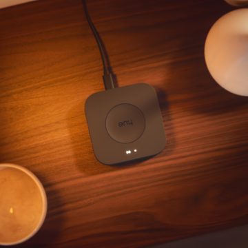 Square smart lighting hub with indicator lights placed on a wooden surface, connected by cable, illuminated by nearby light.
