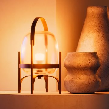 Glass-domed smart lamp with metal handle placed on a shelf, emitting soft light beside two textured ceramic vases.