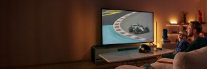 Un père et son fils sourient en regardant une course automobile à la télévision, avec l'éclairage connecté WiZ derrière l'écran et sur les étagères à proximité.