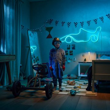 A young boy stands next to a go-kart in his race-themed room, lit by a blue WiZ Smart Flex Strip shaped like a race car.