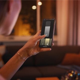 En person, der styrer Philips Hue intelligent belysning ved hjælp af Hue appen på en smartphone.