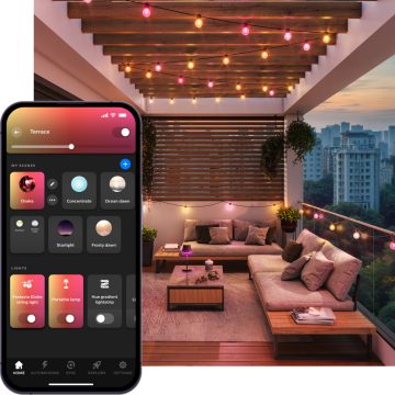 Eine Festavia Globe Outdoor Lichterkette taucht den Sitzbereich eines Balkons bei Nacht in ein smartes Licht aus pinken und gelben Tönen 