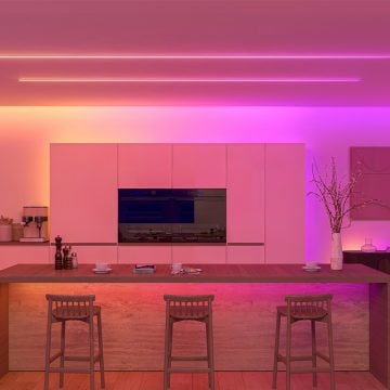 Eine Küche, die in lebendigen Pink- und Orangetönen erleuchtet ist, dank einer Kombination aus verborgenen Lightstrips hinter Deckenblenden und sichtbaren Lightstrips an der Decke. 
