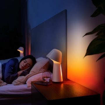 Frau schlafend im Bett mit einer schwach rot und orange leuchtenden Nachttischlampe mit smartem Licht