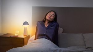 Woman waking up in bedroom with smart wake up light simulating sunrise for a gentle start to the day 