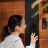A woman at a front door communicating through a Hue wired video doorbell in black. 