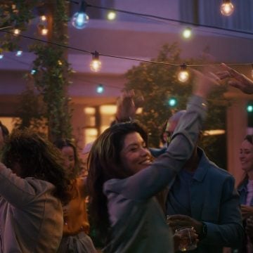 A woman dances on a patio under strings of Festavia outdoor globe party lights glowing in blue, pink, and white smart light.