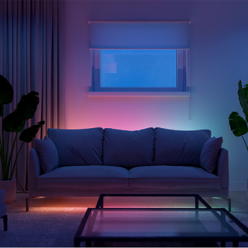 A sofa in a living room illuminated using Essential strip lights creating a wall washing effect in pink and blue tones of light. 