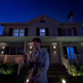 A woman arrives home with the front door and pathway lit with wall lights and pedestal lights. 
