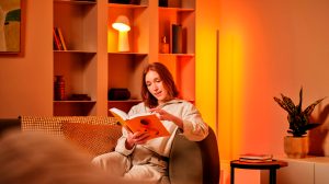 A woman reads a book on the couch, with Hue lamps behind her.
