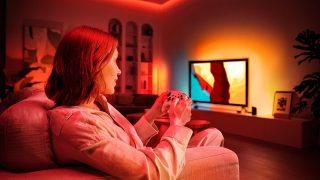 A woman gaming on her TV with an immersive entertainment lighting setup glowing in red, orange, and white smart light. 
