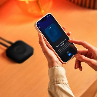 Hand tapping a smartphone screen to set up a smart lighting bridge, with a black bridge device visible on a wooden surface.