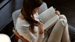 Person reading a book with the best light for reading in a living room chair with bright white light from a lamp illuminating the reading area. 