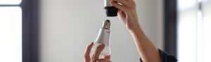 Person's hands installing a white LED light bulb into a ceiling socket, focusing on the bulb and socket connection.
