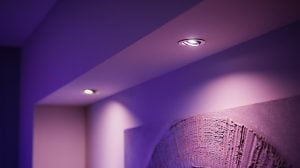 Recessed smart bulbs installed in a ceiling, emitting colored light onto a wall and textured artwork below.