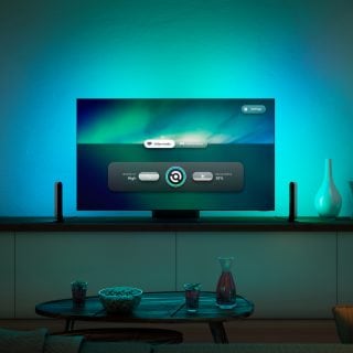 A television on a cabinet with two vertical smart LED bulb lights on each side, casting cool multicolor light onto the wall.