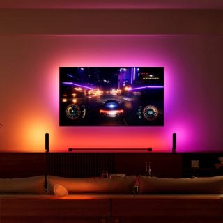 A television mounted on a wall displays a racing video game, with smart home lighting behind the screen matching game visuals.