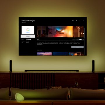 A television mounted on a wall displays the Philips Hue Sync app, with colored light cast behind the screen onto the wall.