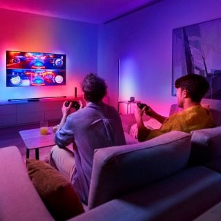 Two people playing video games in a living room with colorful smart lighting synced to the television screen.