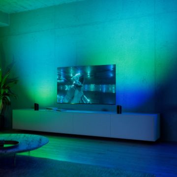 Two play wall washer lamps placed each side of TV and glowing in vibrant green and blue smart light. 