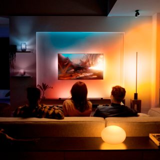 A group of people watching TV in a living room with colorful smart lighting illuminating the walls and shelves, enhancing the viewing experience.