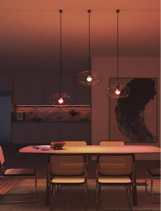 Three Hue Essential smart bulbs fitted to pendant lights with glass shades illuminating a table with pink and warm white light. 