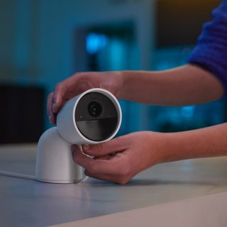 Person adjusting a white security camera on a table, positioning the device for optimal indoor monitoring.